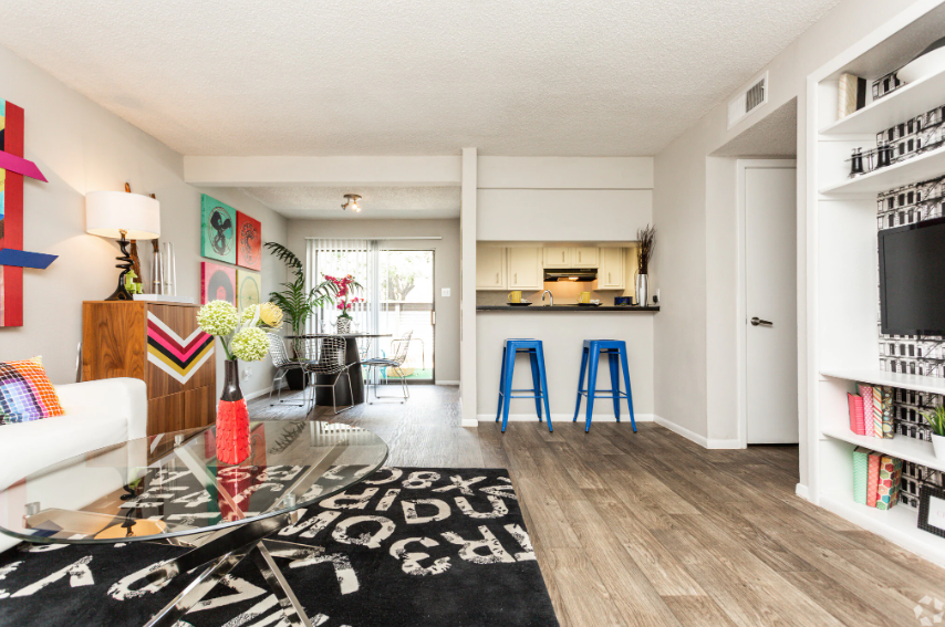 Bright open-plan living room with colorful decor, kitchen island with blue stools, and large window.