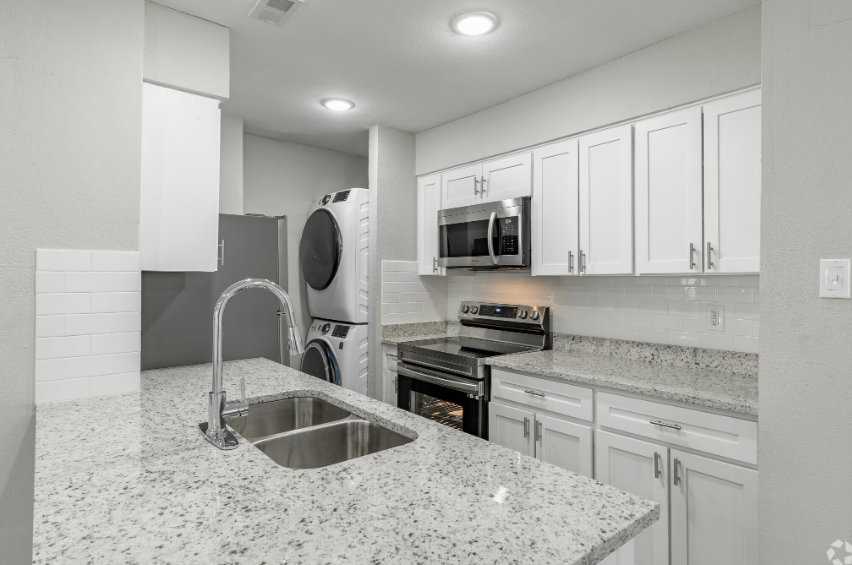 Bright white kitchen with granite island, stainless appliances, and laundry nook in the background