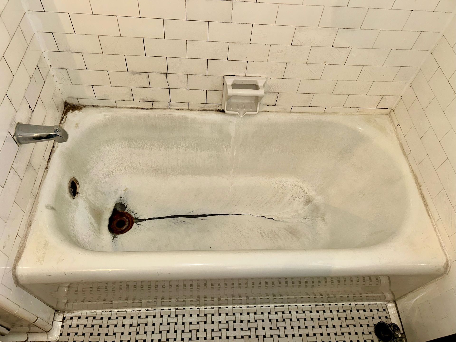 Picture of an older bathtub that has mold stains and rust on the tub and the tile.