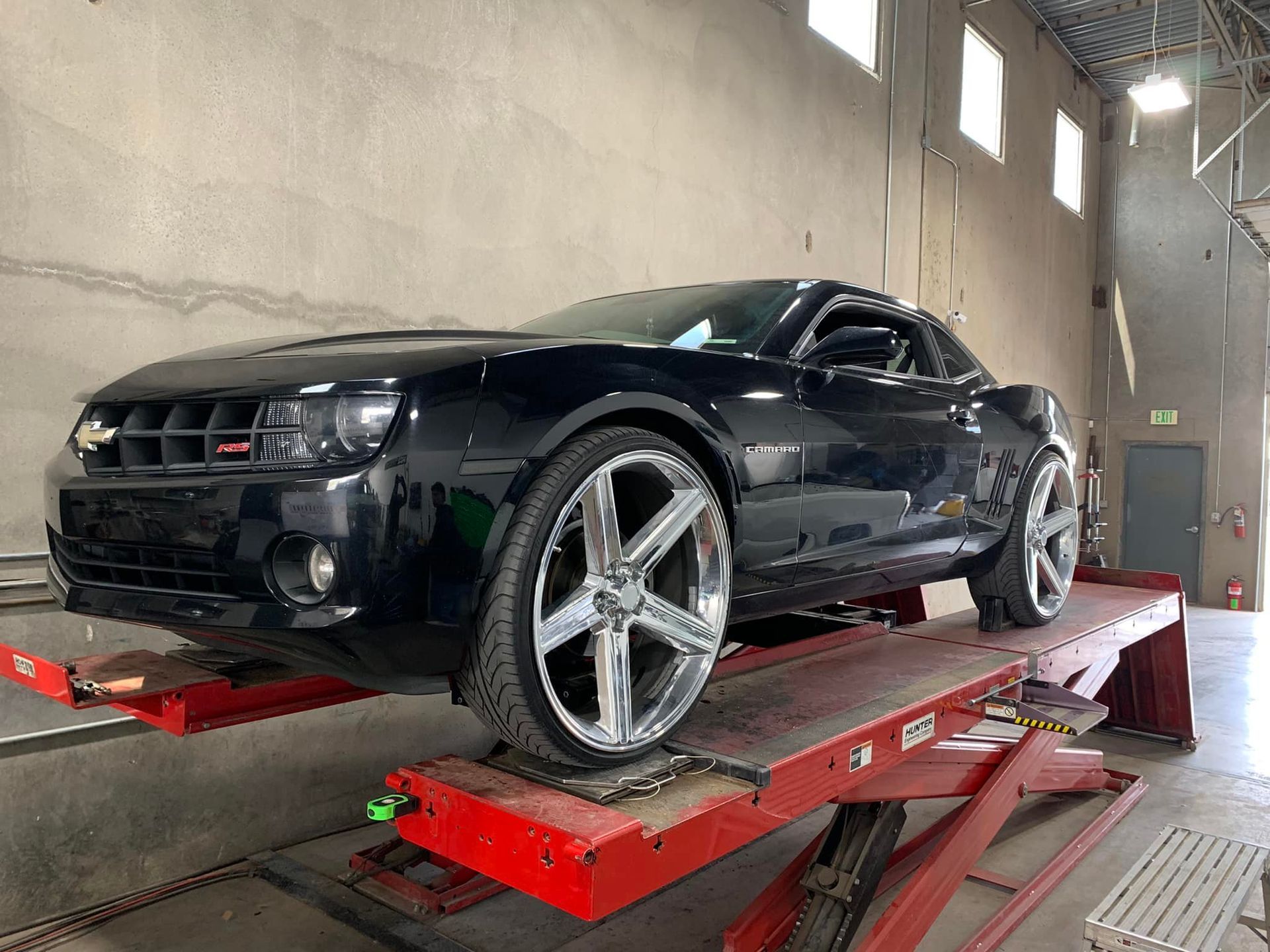Black Chevy Camaro on a red hydraulic lift inside a garage.