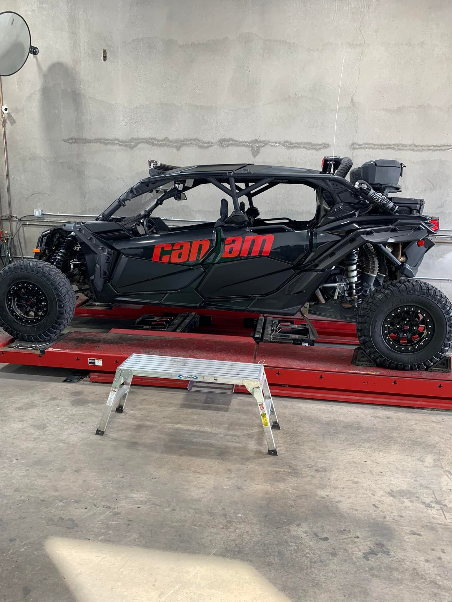 Black Can-Am off-road vehicle on a red lift inside a garage. A small step stool is in front.