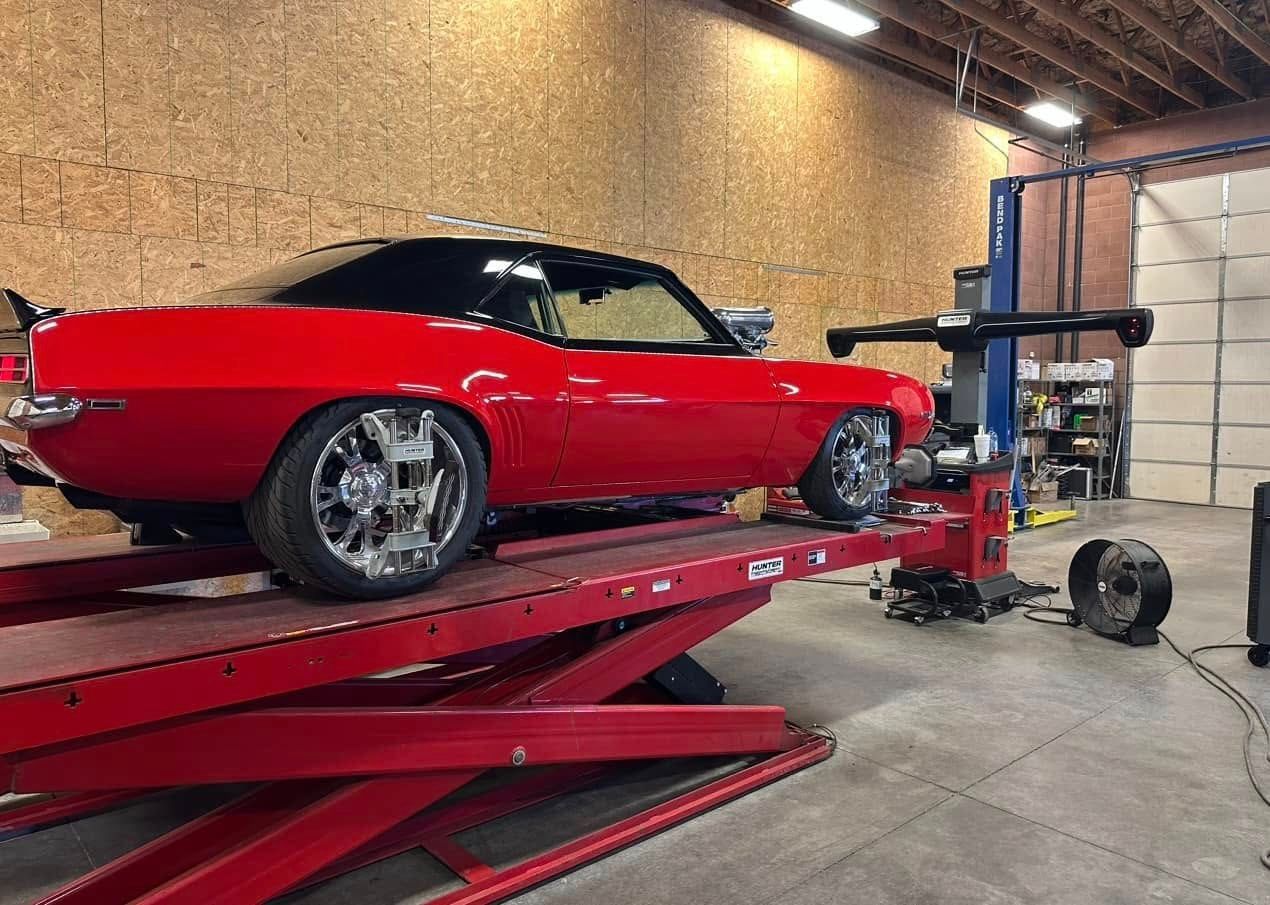 Red classic car on a red lift in a garage, with alignment equipment attached to wheels.