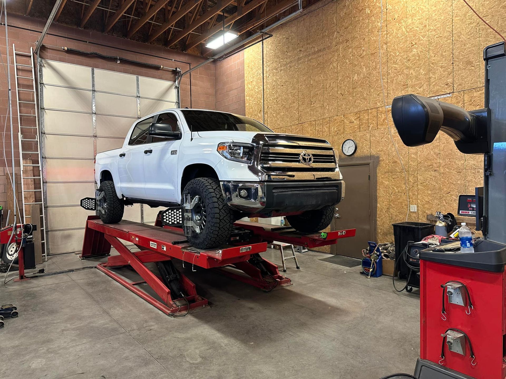 White pickup truck on a red lift in a garage, undergoing an alignment.