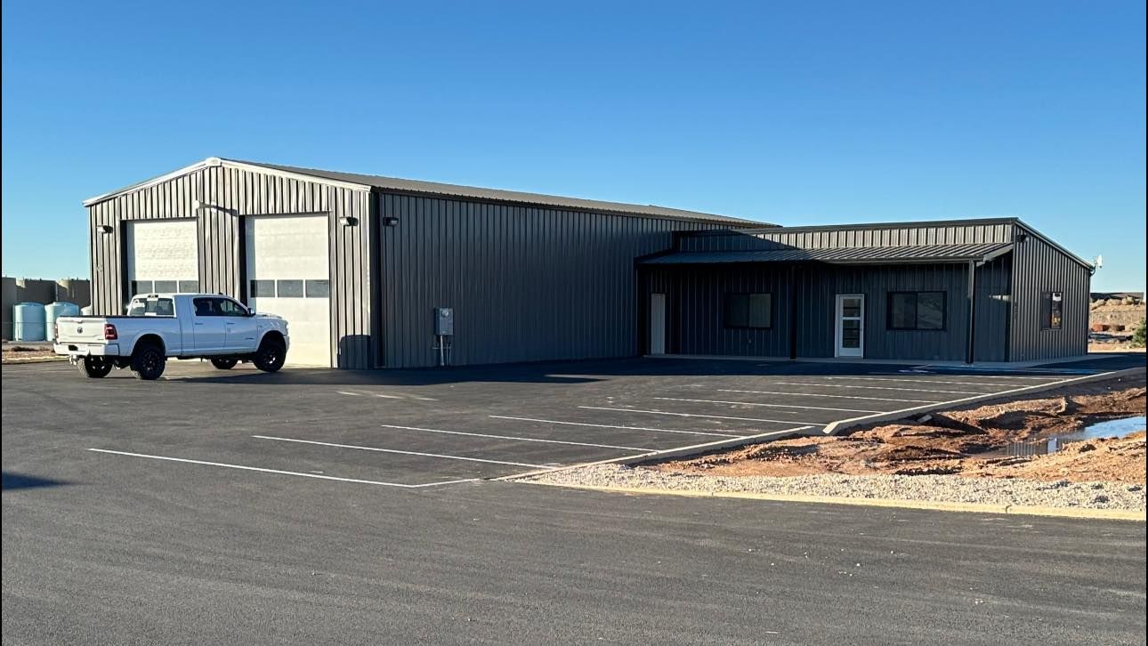 A gray metal building with two garage doors and a white pickup truck parked outside on a paved lot.
