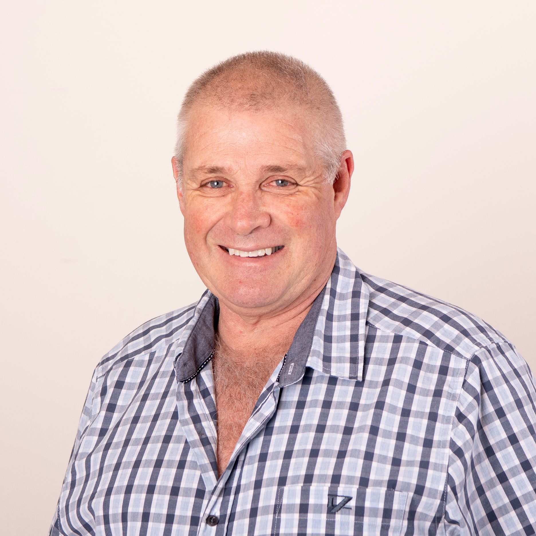 Man with short hair smiles, wearing a blue and white checkered shirt, against a white background.
