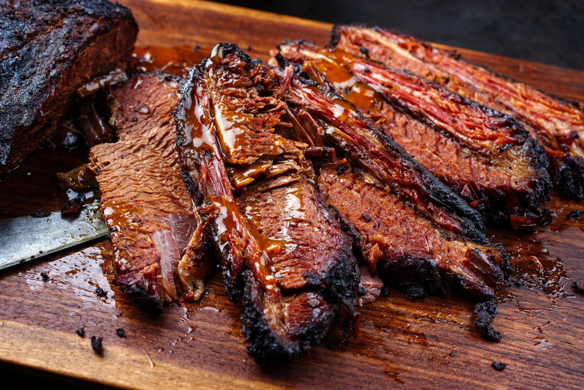 Sliced, smoky brisket on a wooden cutting board, glistening with sauce.