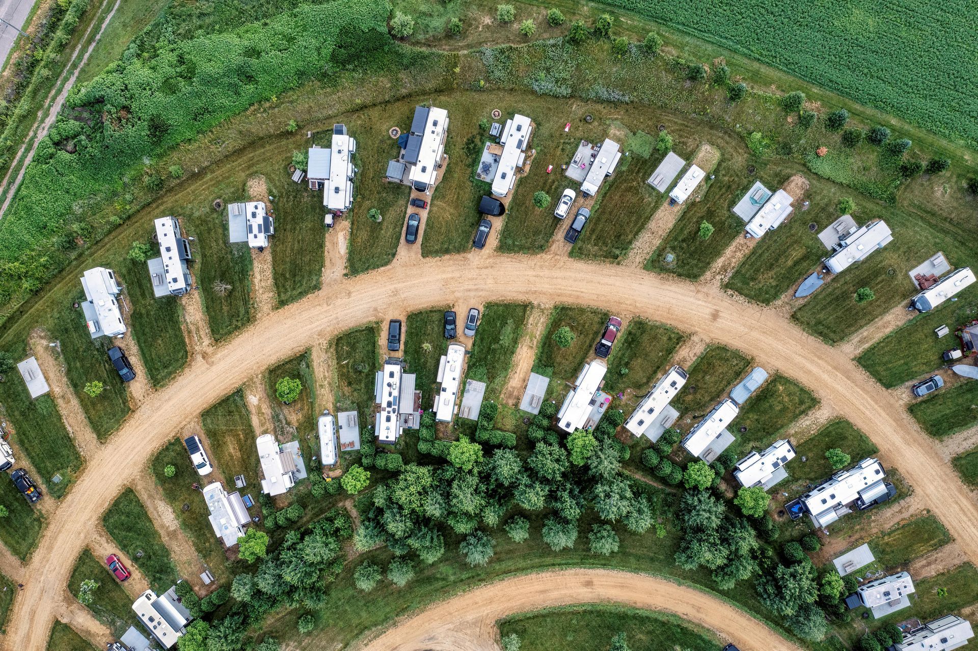 Aerial view of RV campground with parked trailers on dirt lots surrounded by green grass.