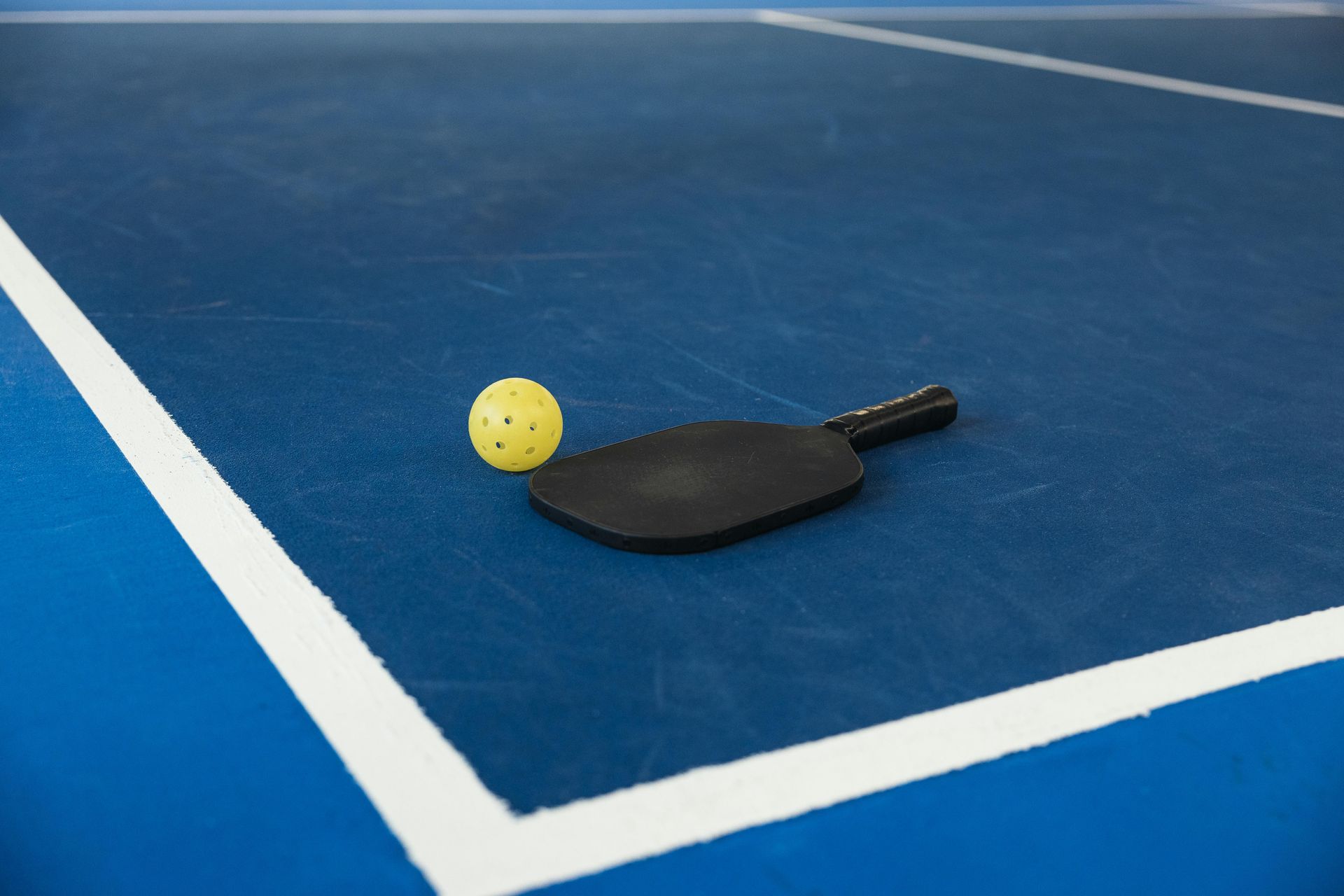 Pickleball paddle and ball on a blue court, near white lines.
