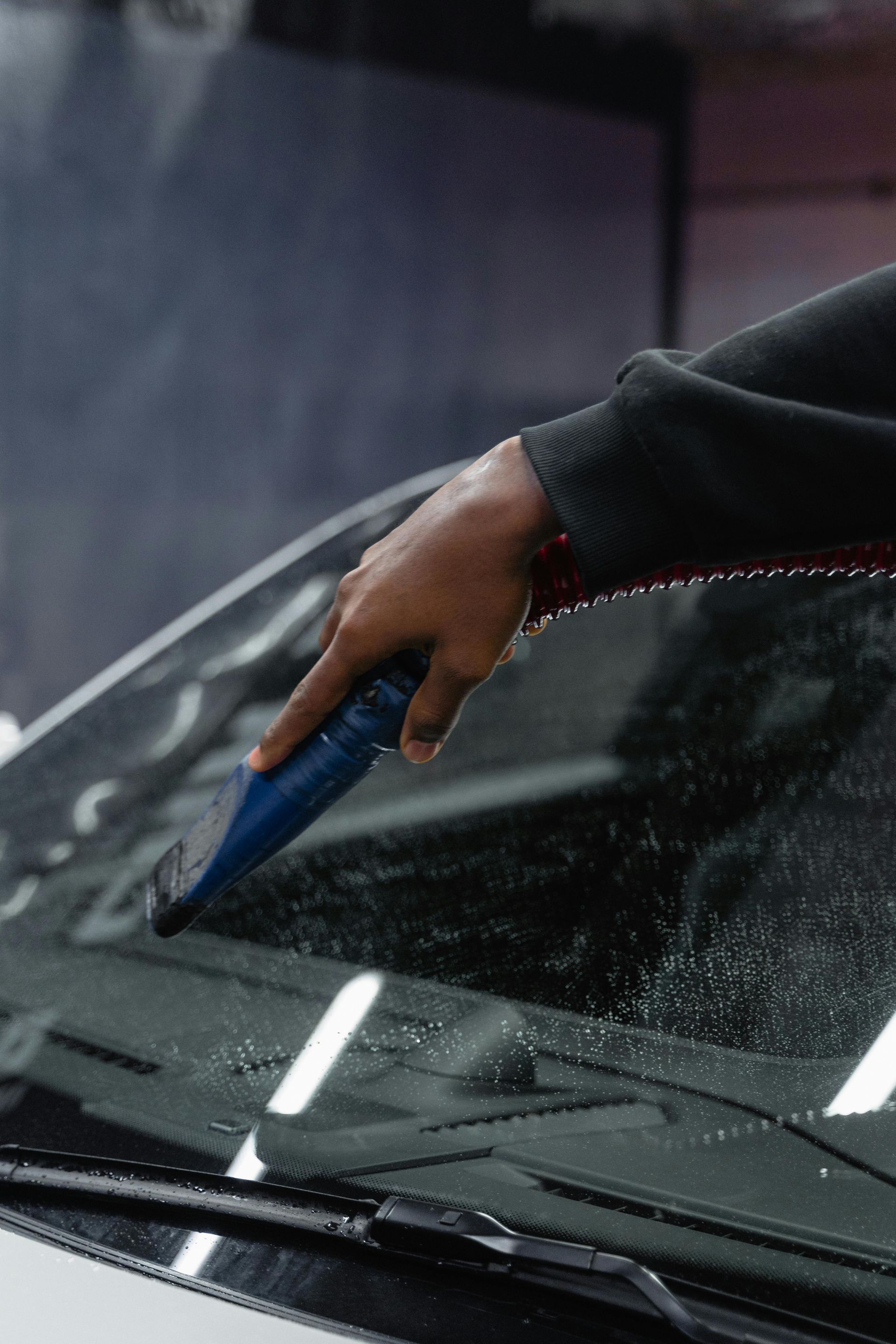 A person is cleaning the windshield of a car with a brush.