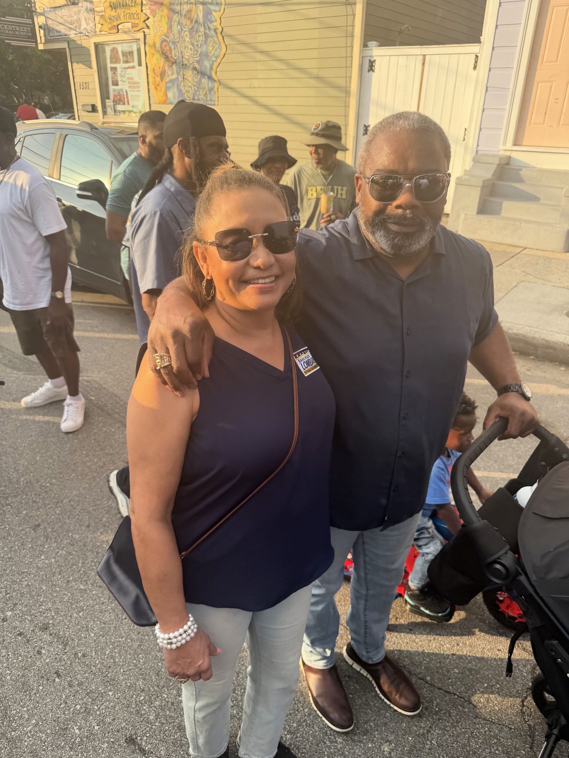 Two people smiling outdoors, standing on a street beside a stroller.