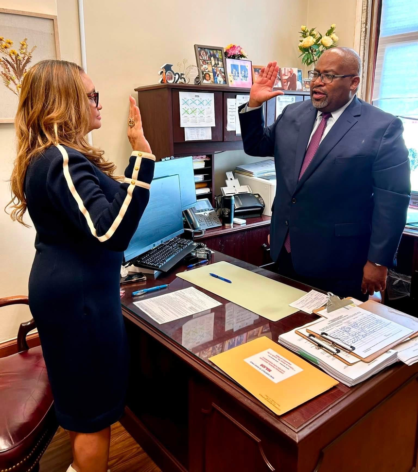 Two people in an office raising hands during a meeting beside a wooden desk.