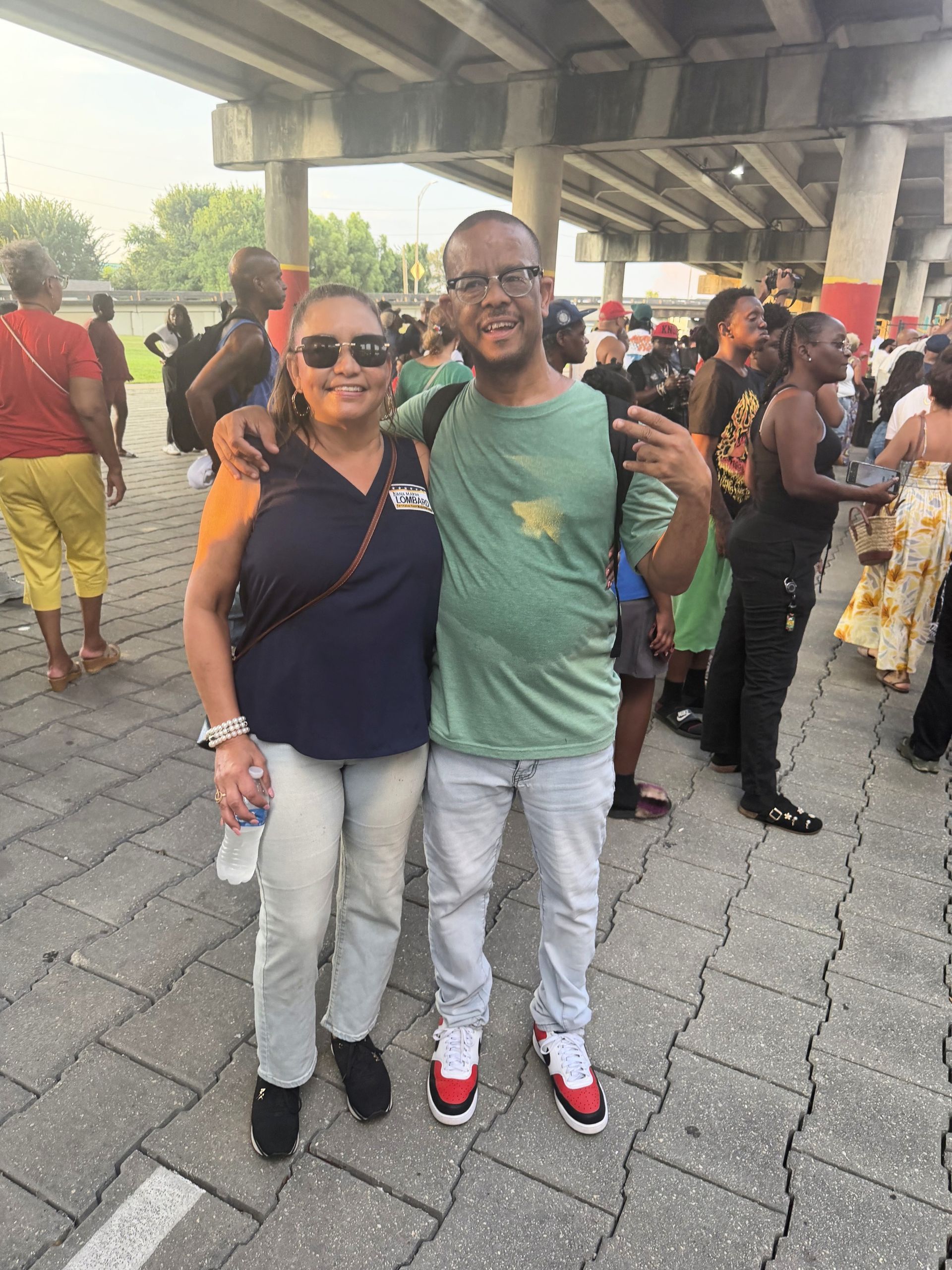 Two people smiling outdoors under an overpass, standing close together in a crowd.