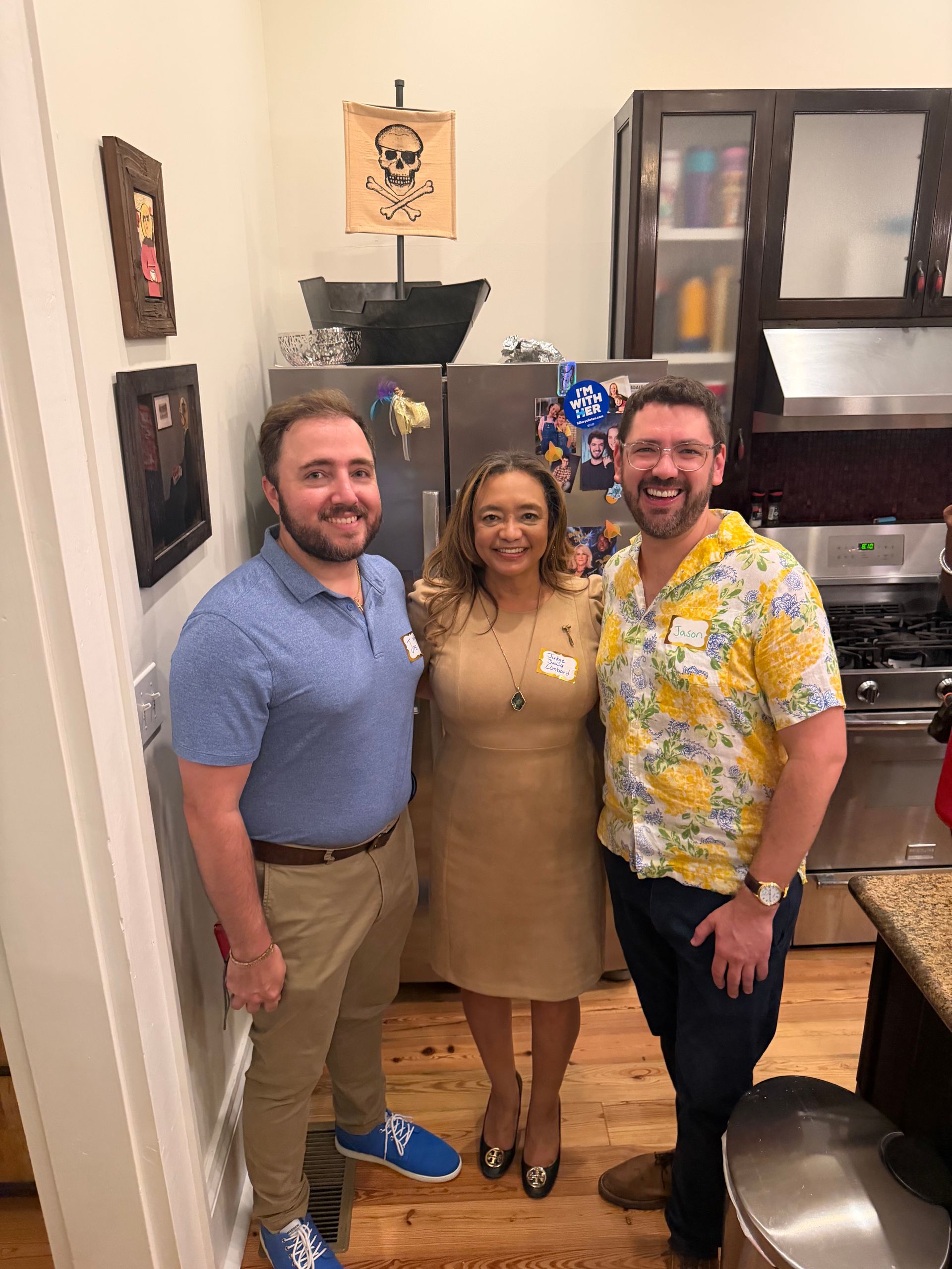 Three people smiling in a kitchen, standing together near a counter.