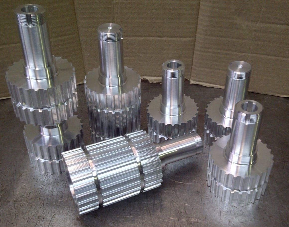 Varias piezas metálicas brillantes y mecanizadas, con bordes en forma de engranaje, dispuestas sobre una superficie.