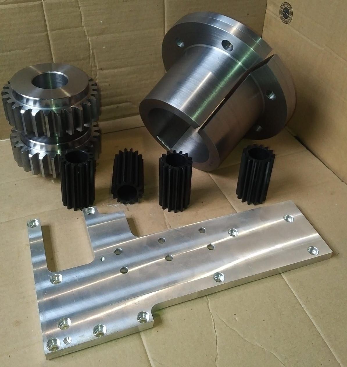 Piezas mecánicas: engranajes, carcasa de cojinetes, placa de aluminio, todo ello en una caja de cartón.