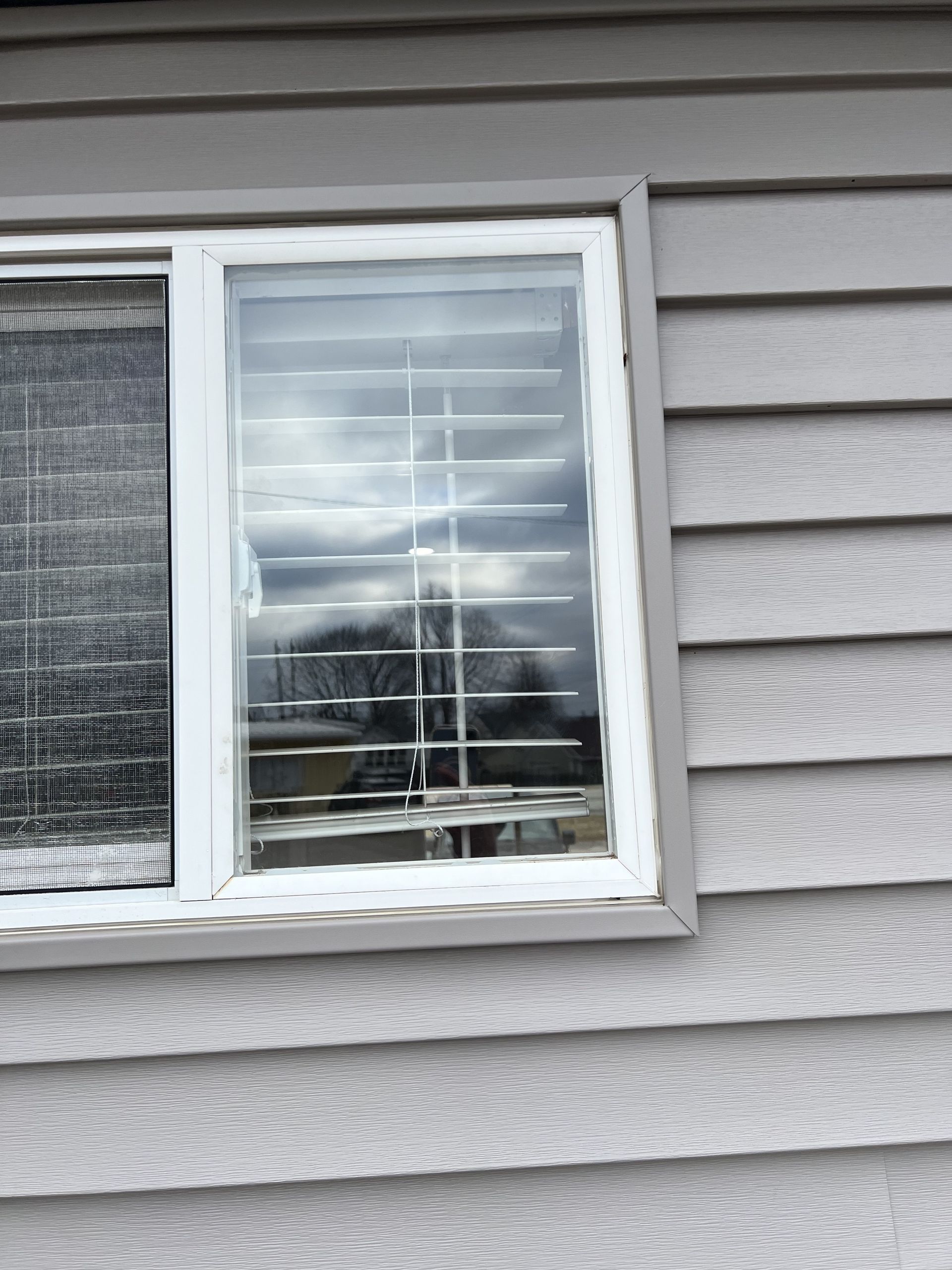 A window with blinds on it is on the side of a house.