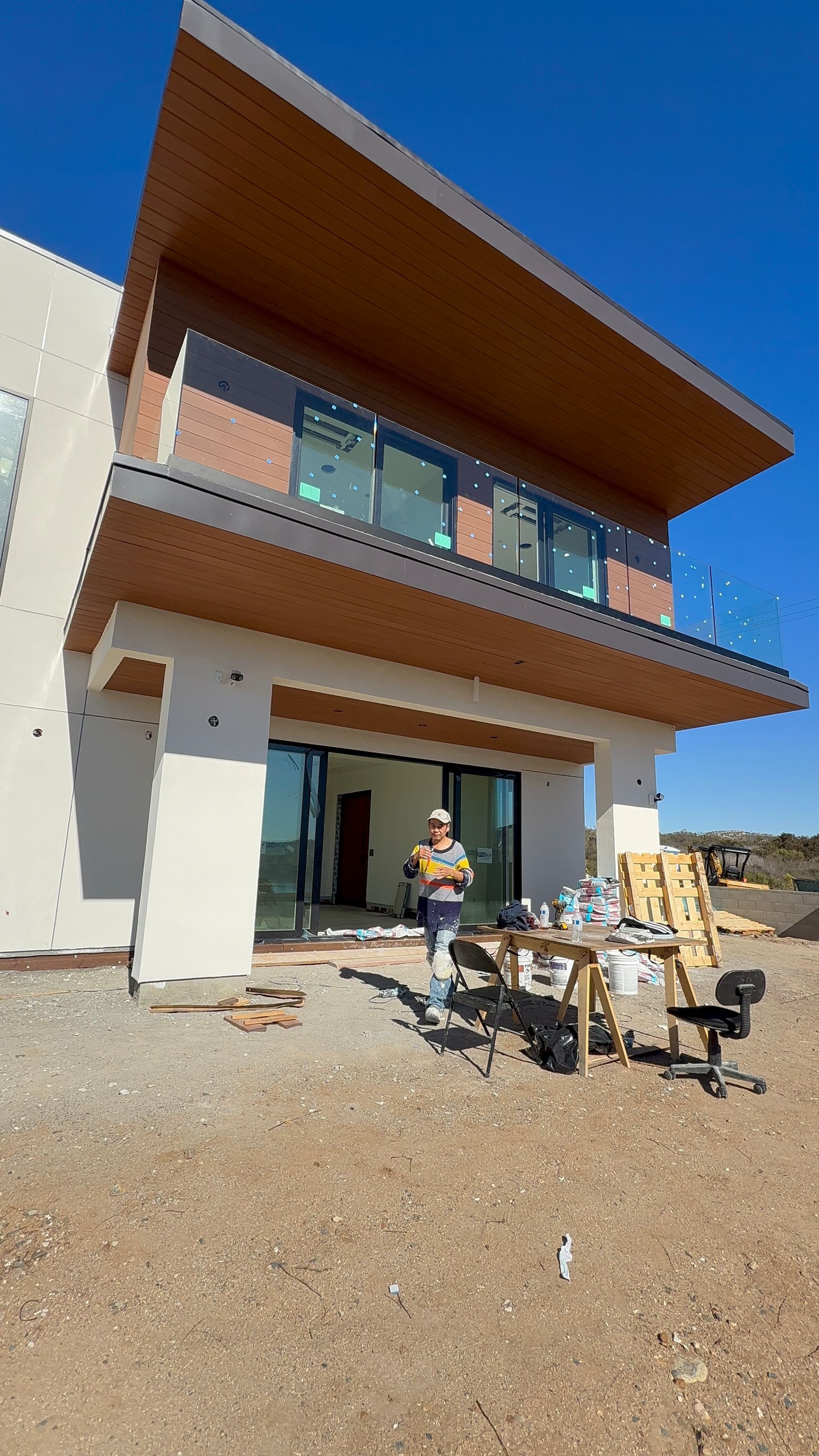 A person in a blue shirt and cap installs a window screen on the exterior of a stucco home.