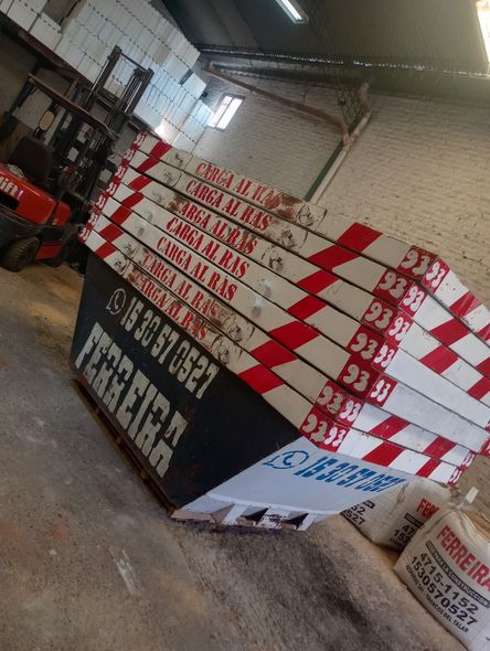 Cajas impresas en rojo y blanco apiladas en un pasillo de un almacén junto a un letrero negro.