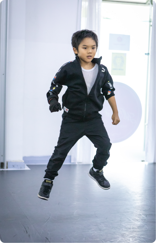 A young boy in a black jacket and black pants is jumping in the air.