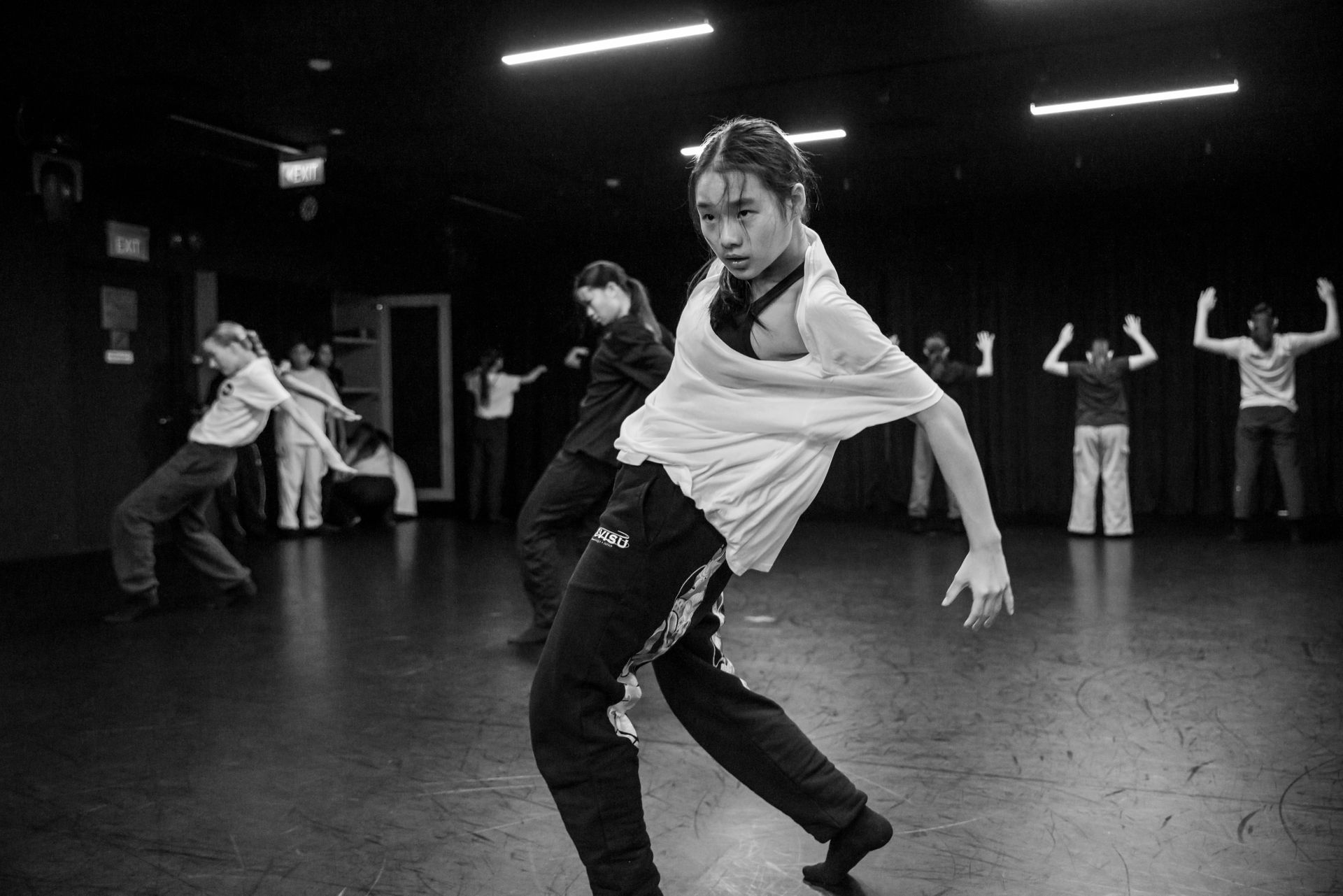 A group of dancers practices in a studio, with one person in the foreground mid-movement during a contemporary dance.