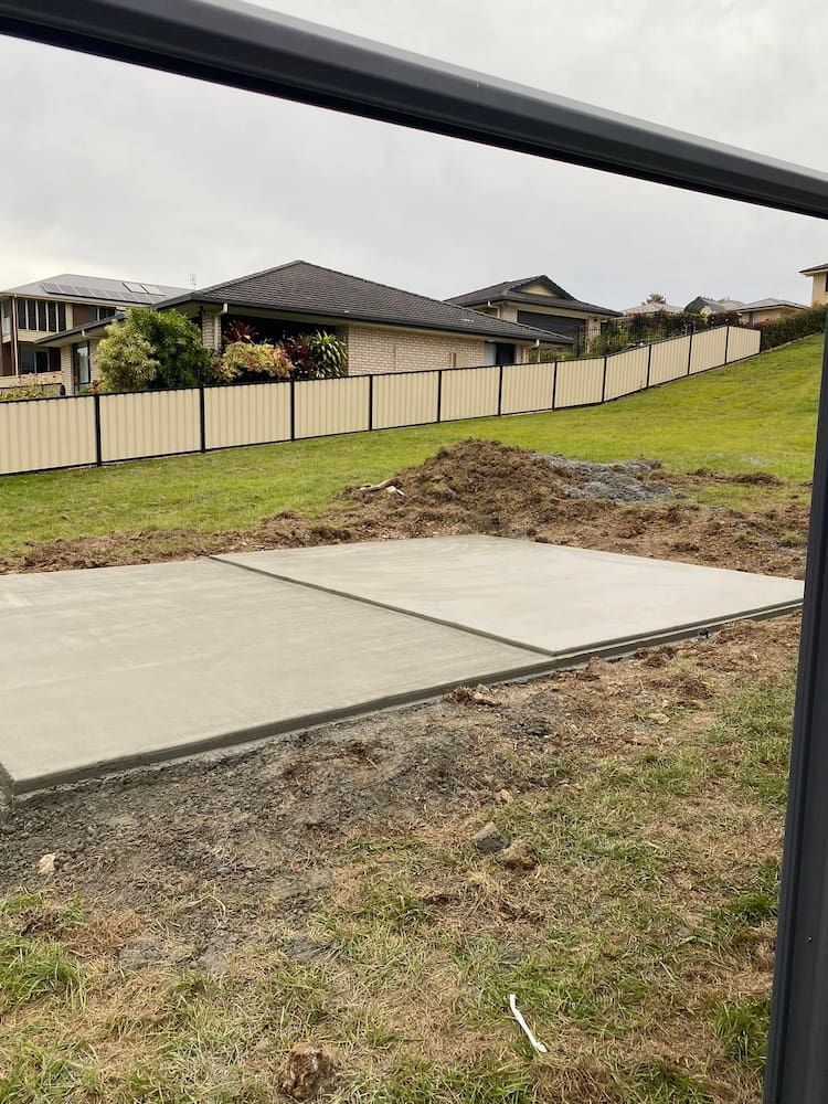 Concrete Patio in a Backyard, Dirt Mound, Beige Fence, Overcast Sky — JDC Concreting in Grafton, NSW