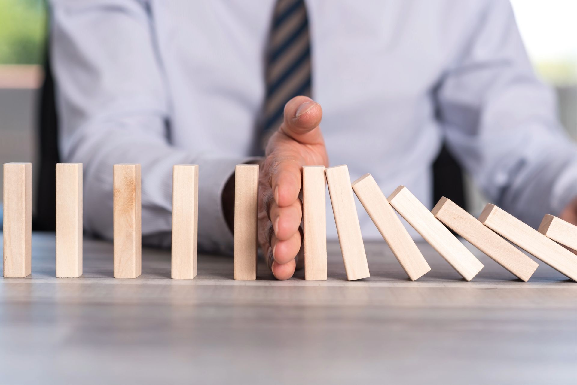 Hand stopping a row of falling dominoes on a table.