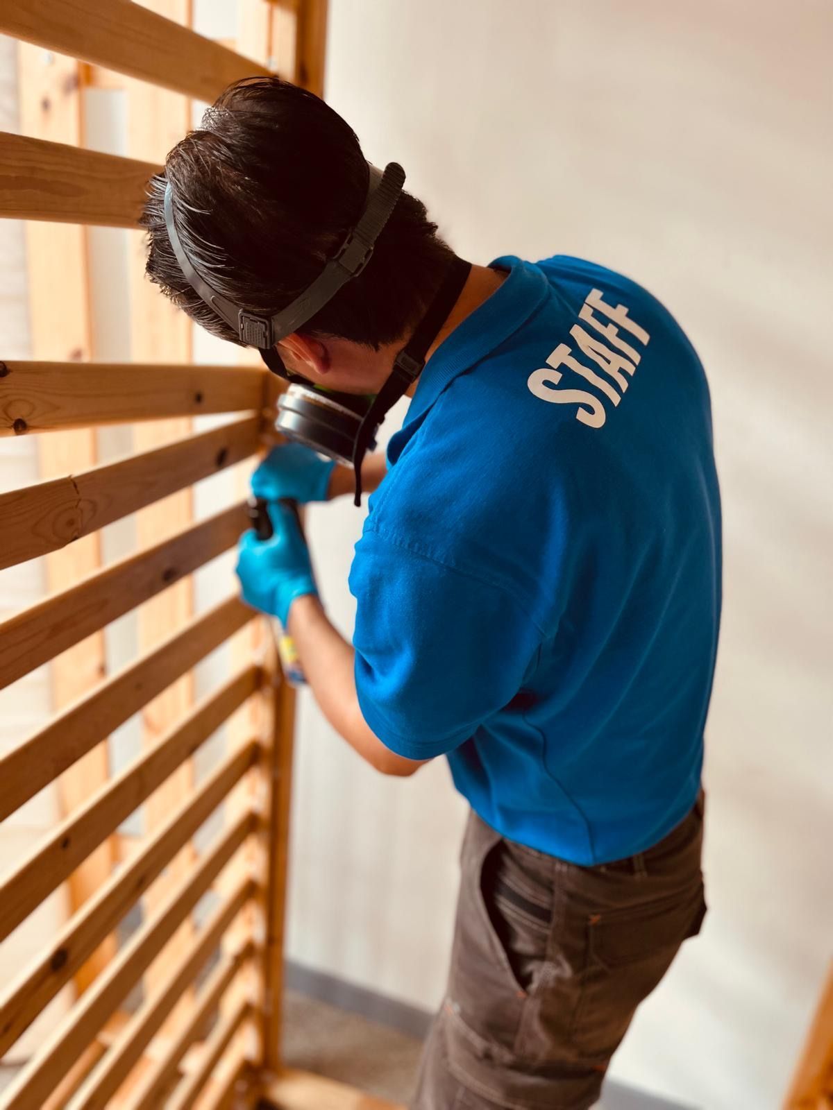 Un membro dello staff, con indosso una camicia blu e guanti, fora delle assi di legno su una scala.