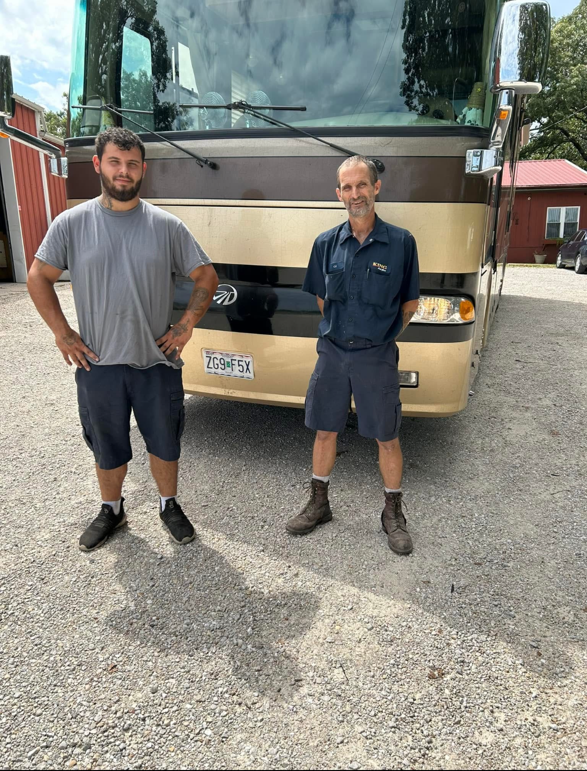 Two men standing in front of a beige tour bus on a gravel lot