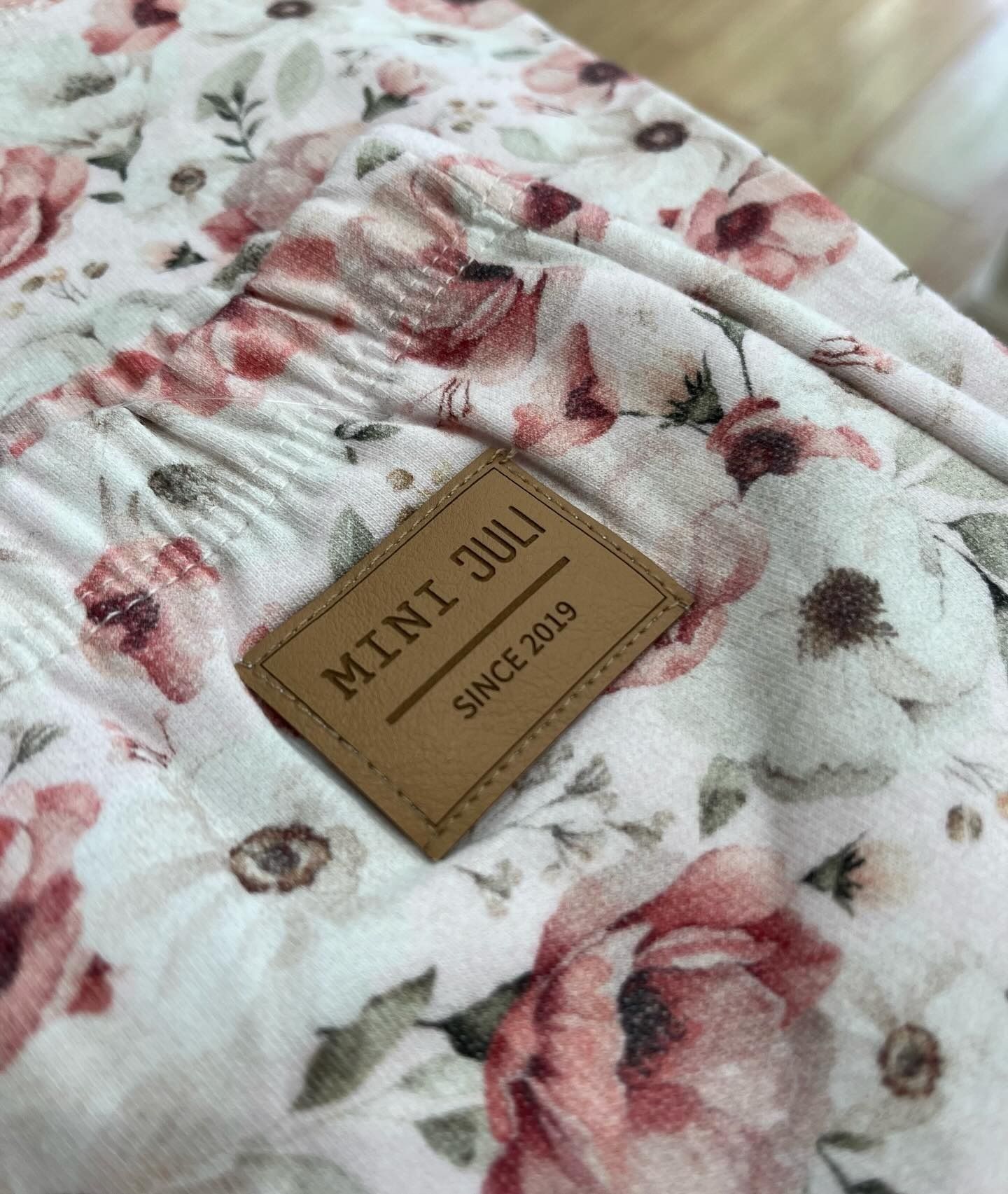 Tela acolchada con estampado floral y una etiqueta de cuero color canela con las inscripciones “MINI JULI” y “SINCE 2018”.
