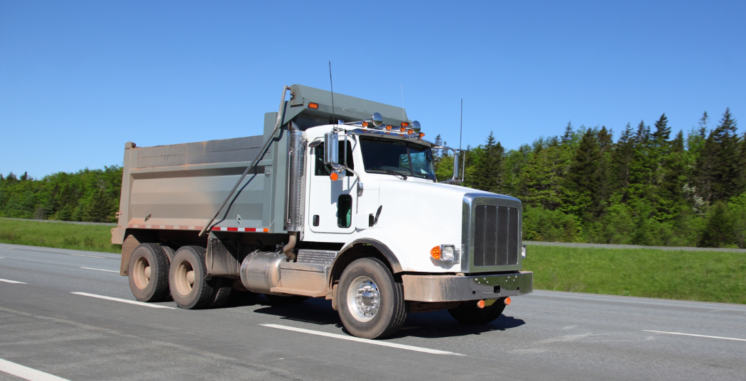A white dump truck is driving down a road.