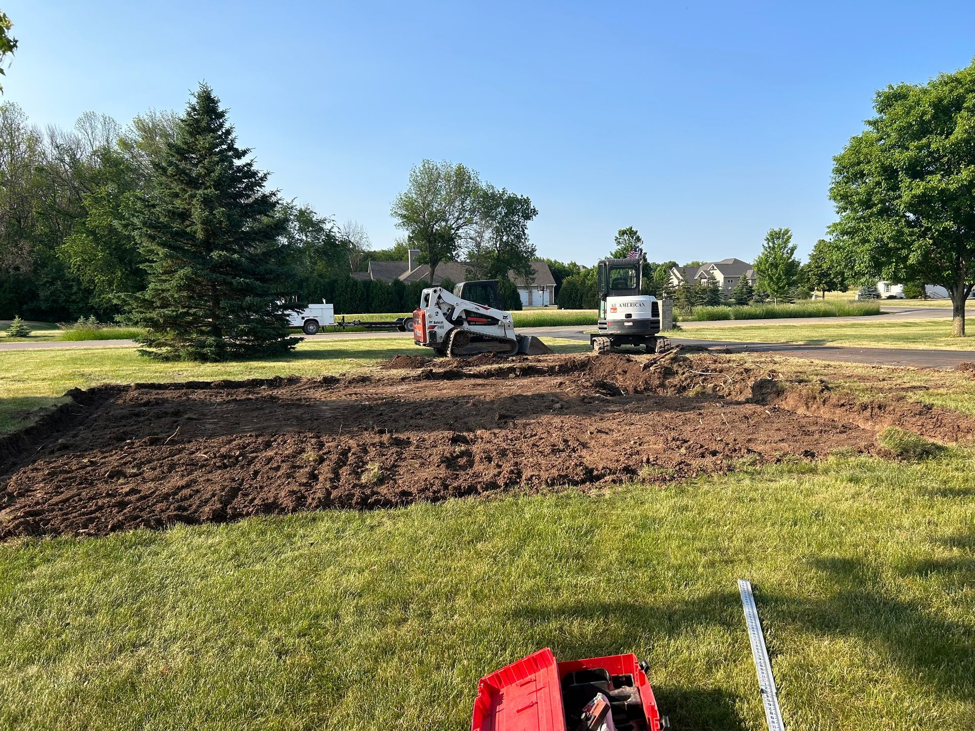 A bulldozer is digging a hole in the grass in a yard.