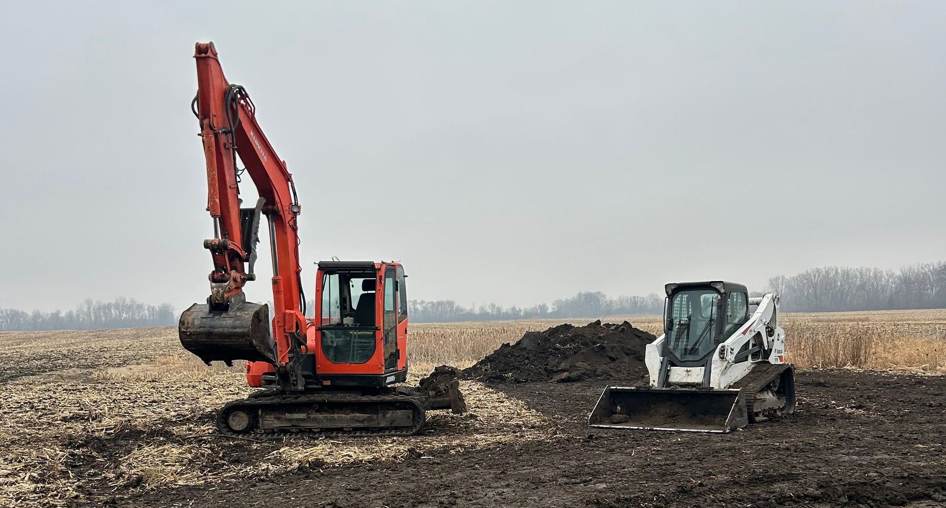 A bulldozer and an excavator are working in a field.