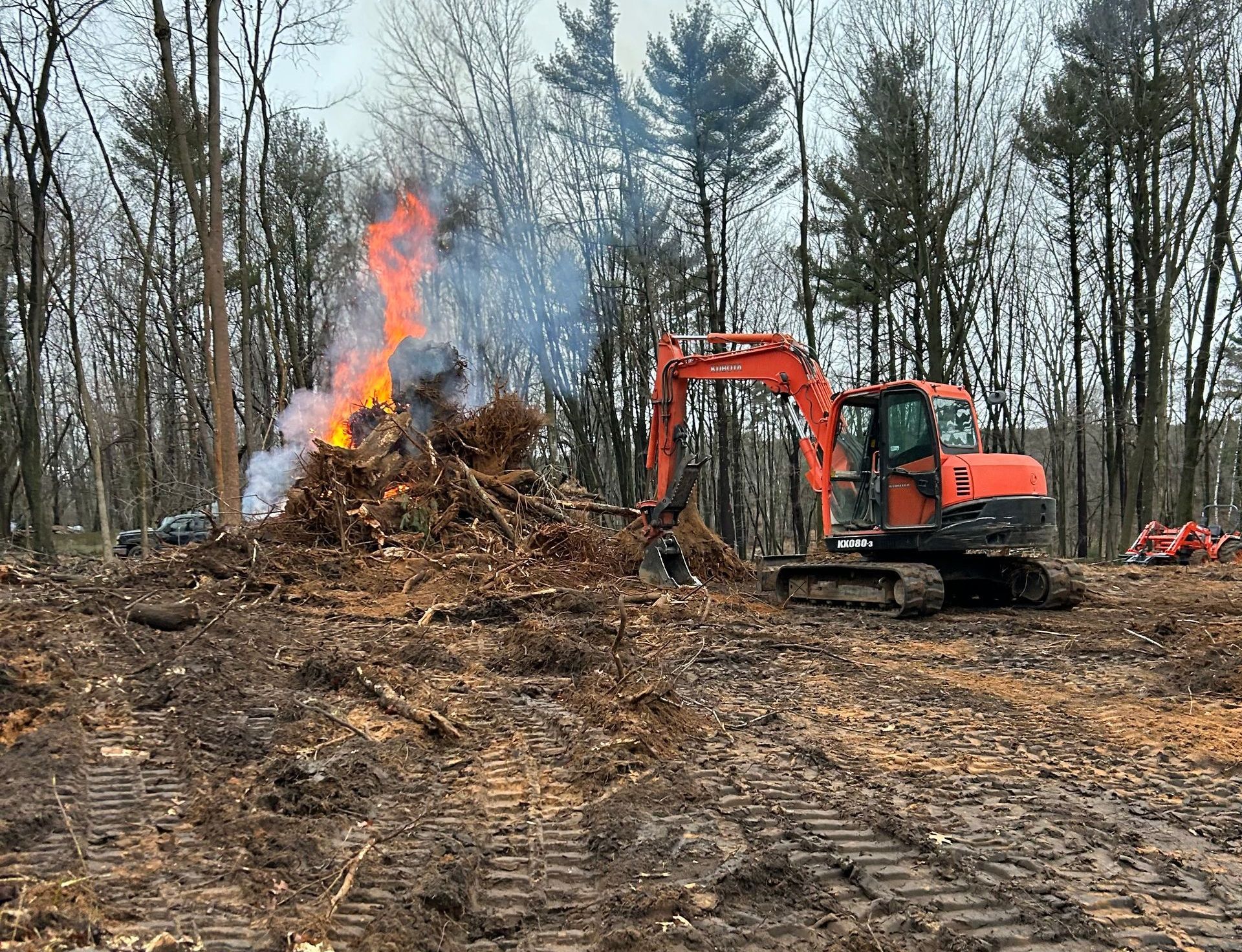A bulldozer is moving dirt in a field with a fire in the background.