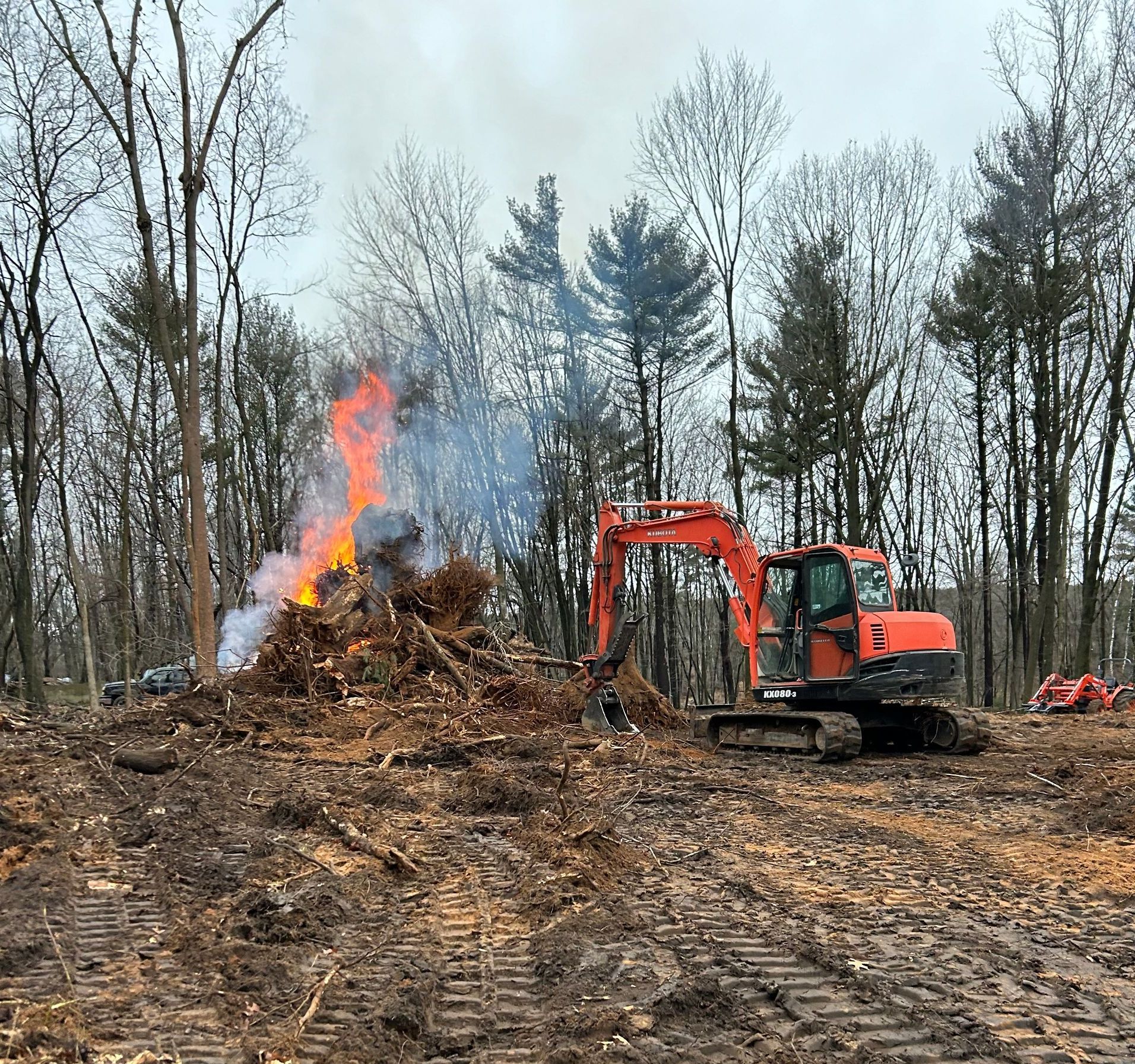 A bulldozer is working in a field next to a pile of wood and a fire.