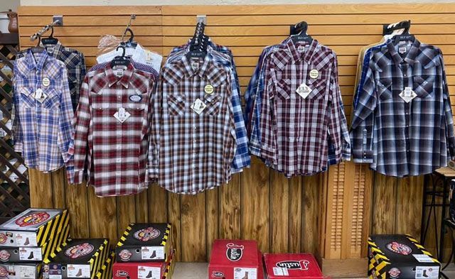 Shirts and boots for sale: plaid button-downs hang above rows of boot boxes, displayed on wooden shelves.