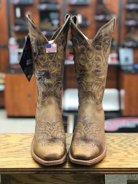 Pair of distressed leather cowboy boots with decorative stitching and an American flag tag.