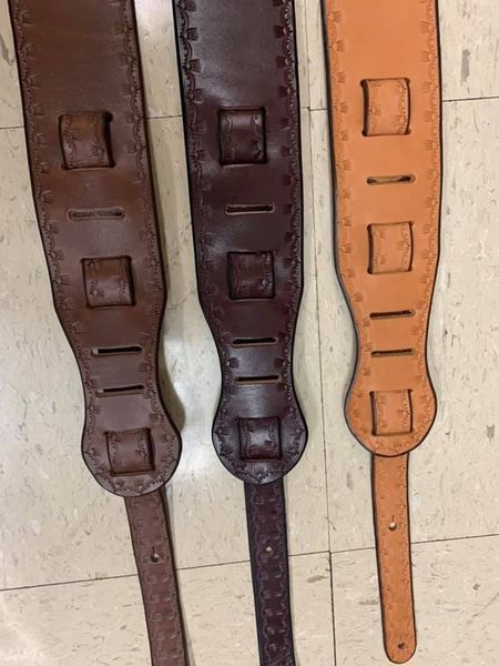 Three leather guitar straps in varying shades of brown, displayed on a floor.