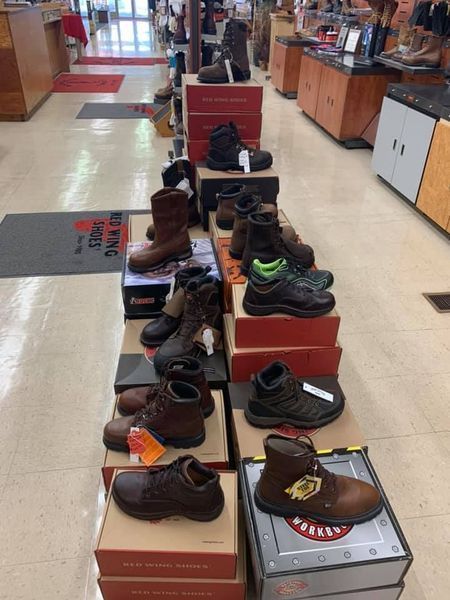 Rows of work boots displayed on boxes in a store; various styles and colors visible.
