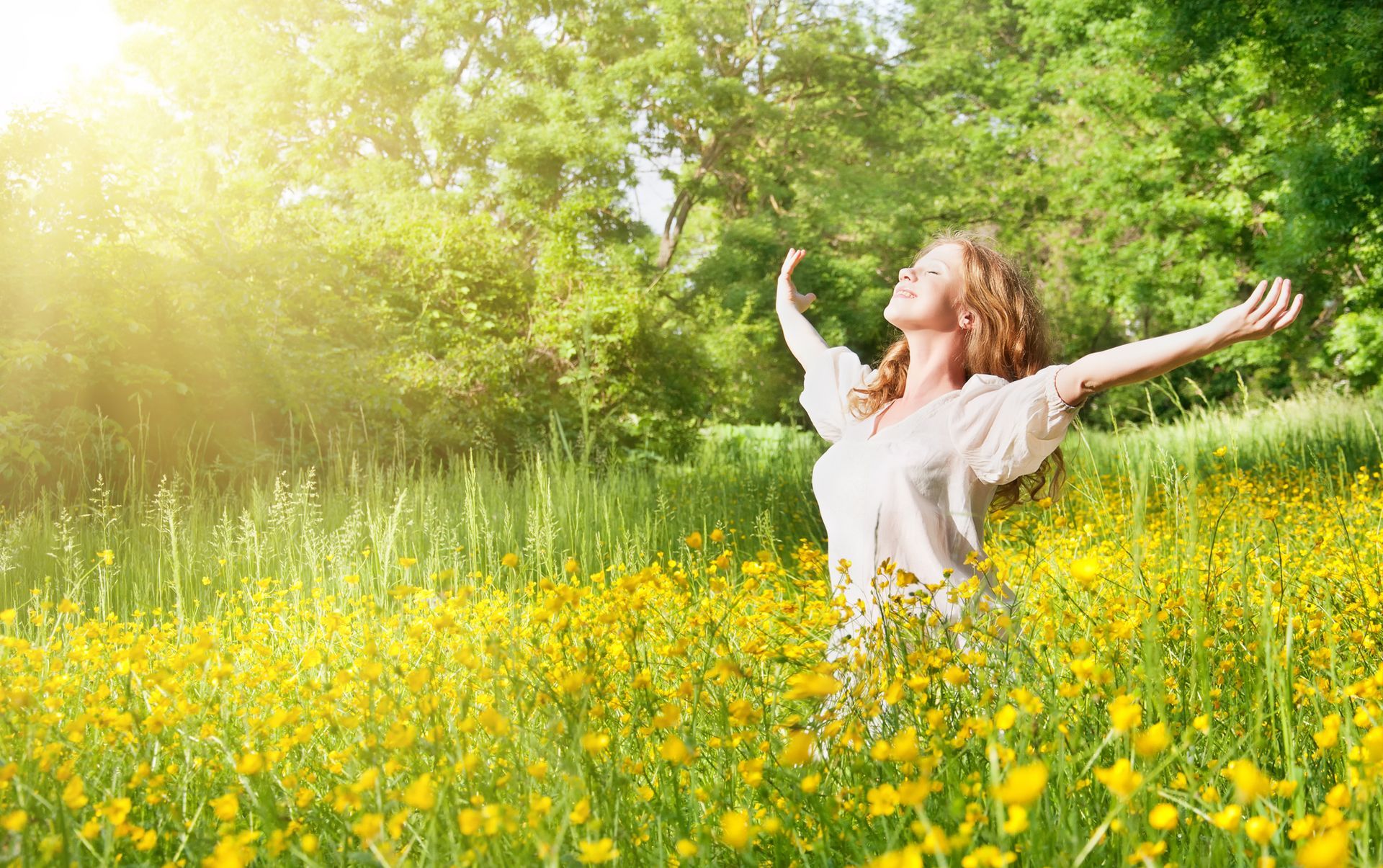Woman with arms raised, silhouetted against a colorful sunset over a grassy field, expressing joy.