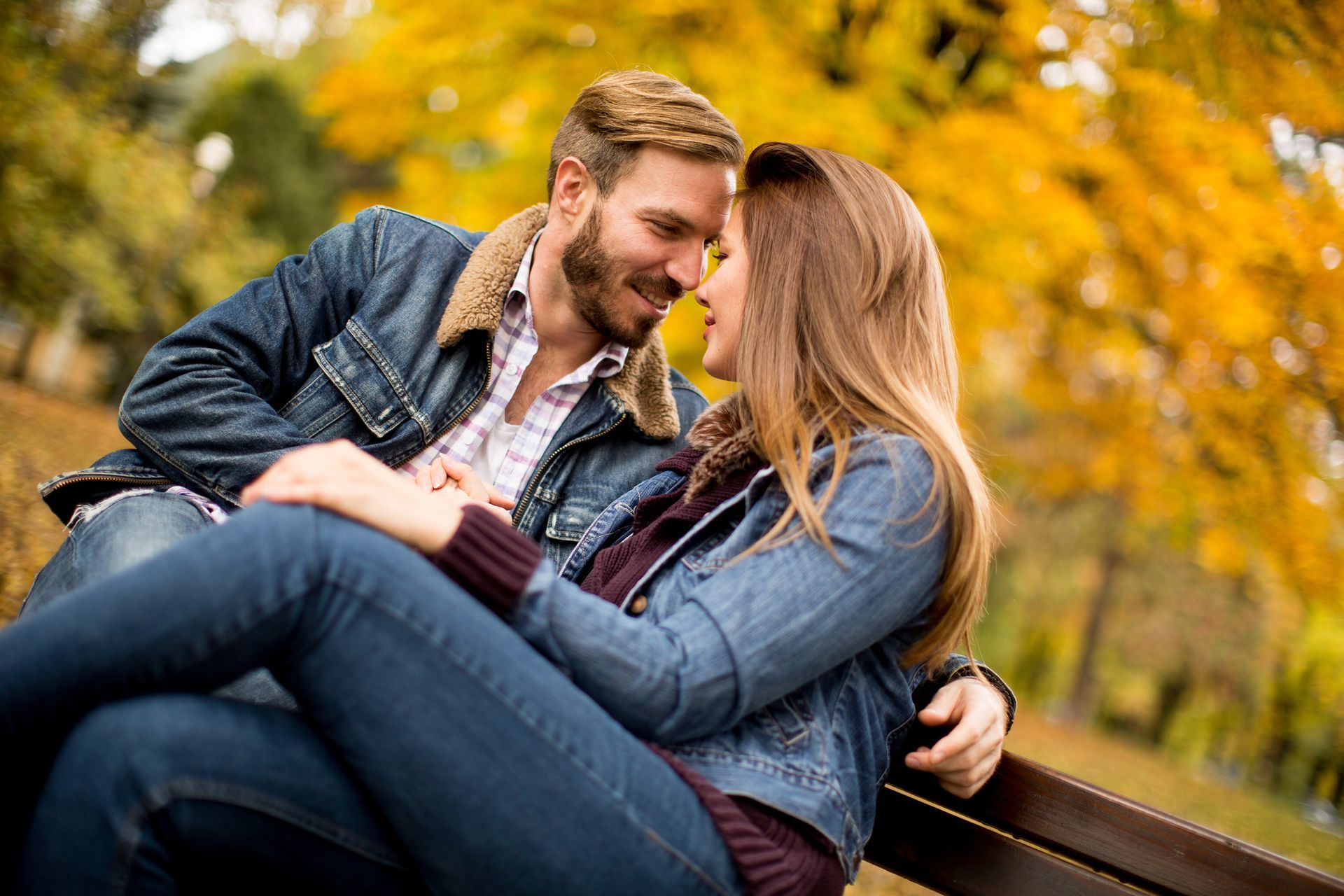 Emotioneel verbonden stel op een bankje in een herfstbos en kijkt elkaar liefdevol aan-relatie