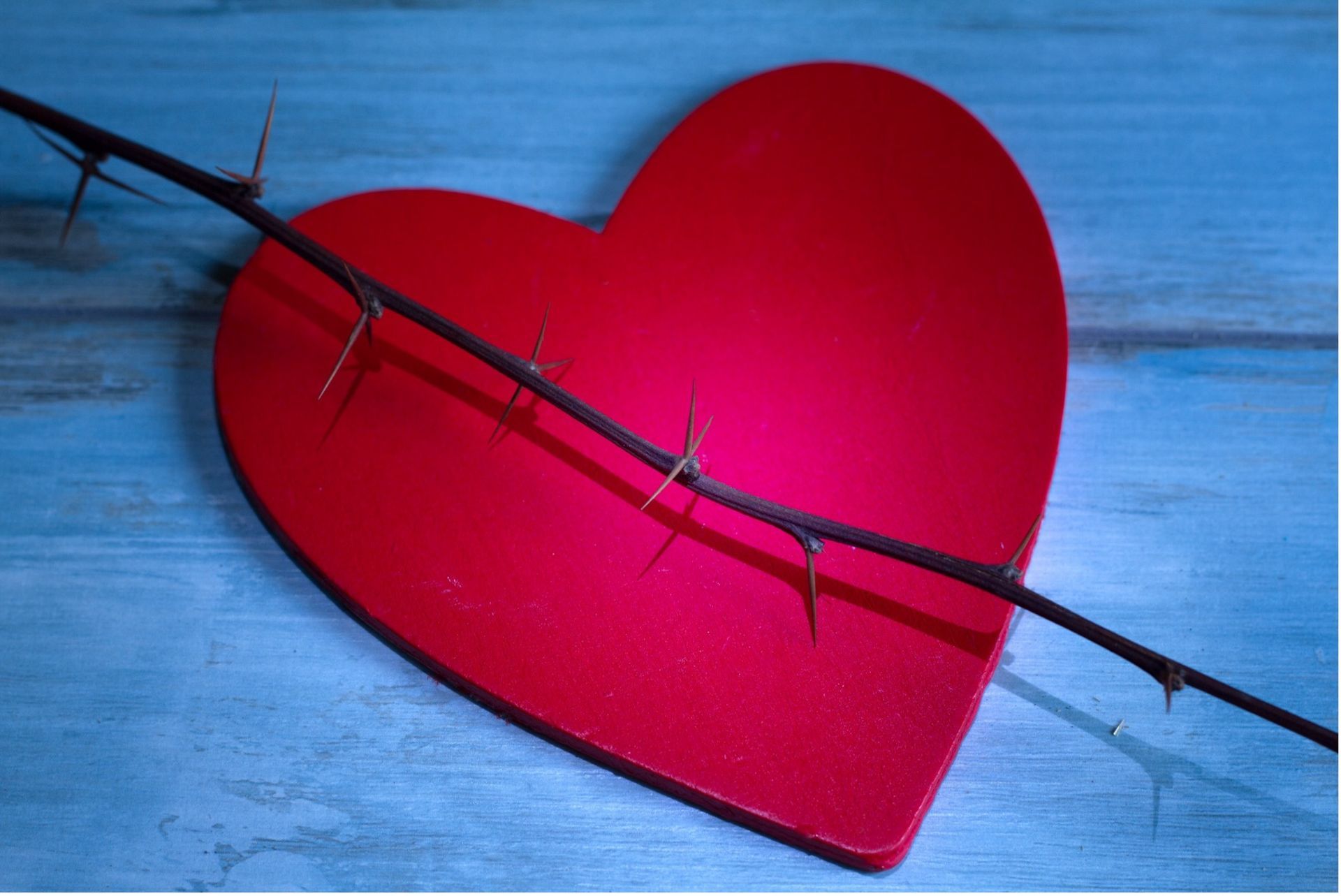 Red heart pierced by a thorny branch on a blue background, symbolizing heartbreak.