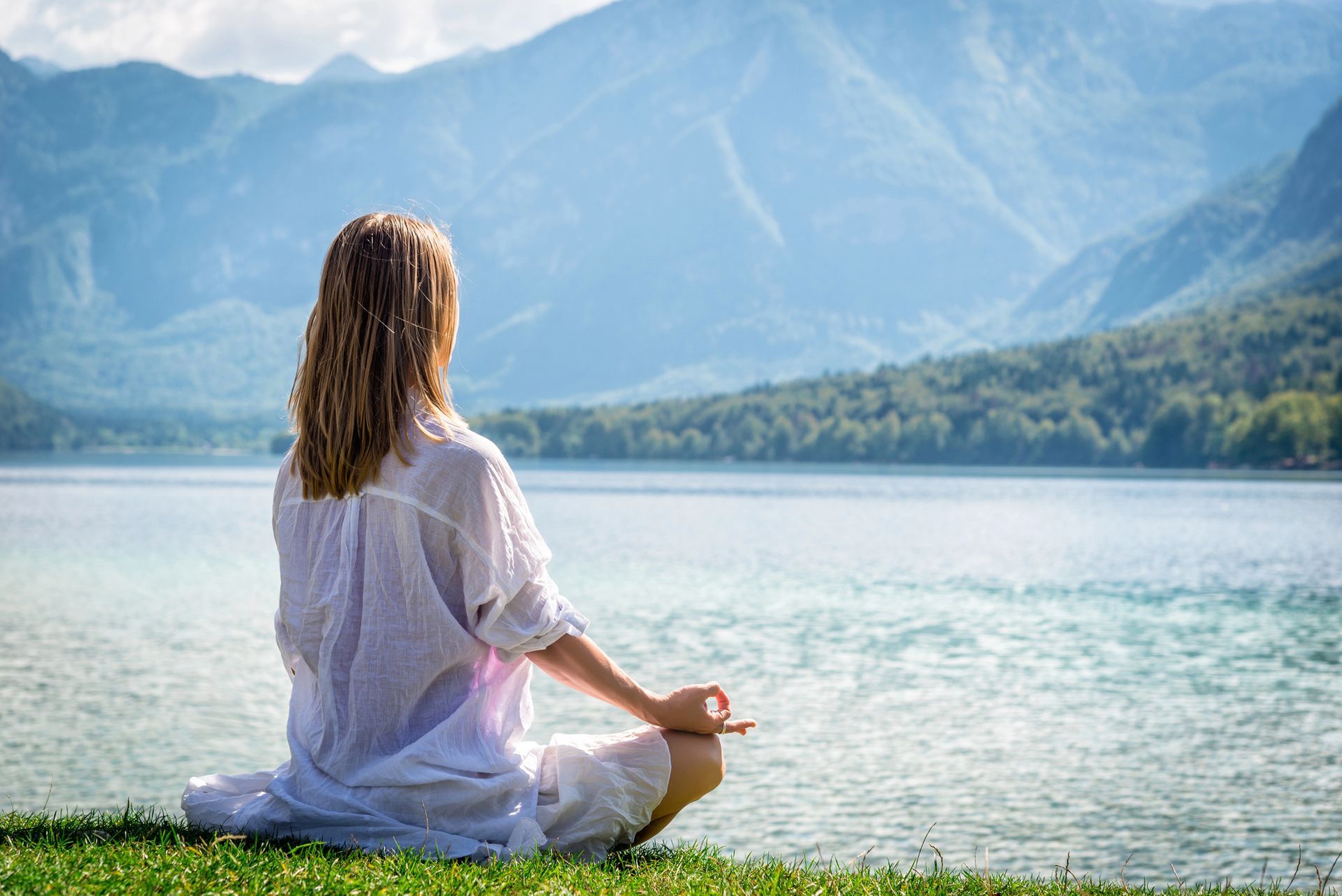 Woman meditating by a lake with mountains in the background.