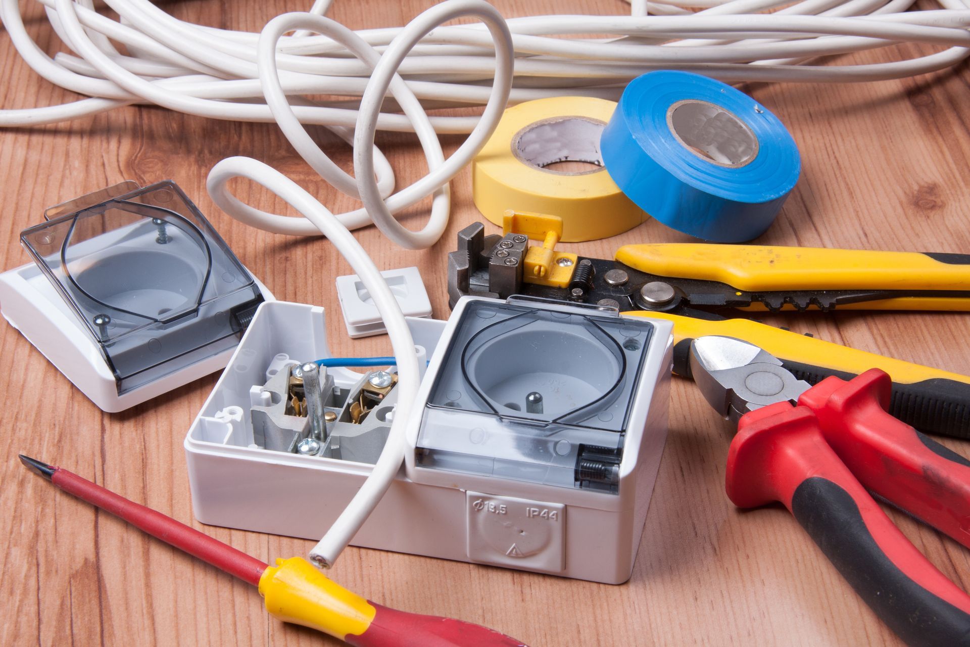 Electrical tools, including wire strippers, pliers, and a screwdriver, alongside wiring components on a wooden surface.