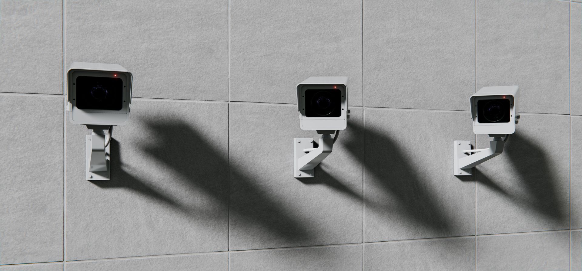 Three wall-mounted security cameras casting long shadows on a tiled surface, monitoring an area.