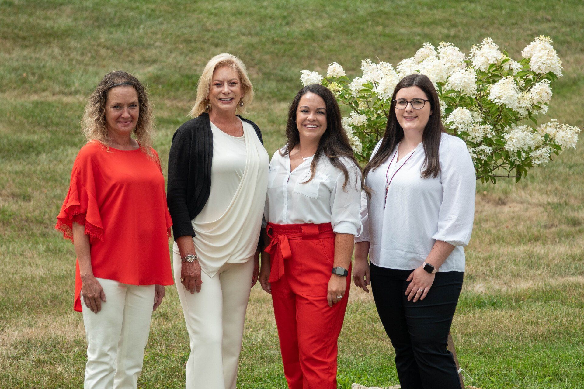 Four people standing outdoors by white flowers, smiling at the camera.