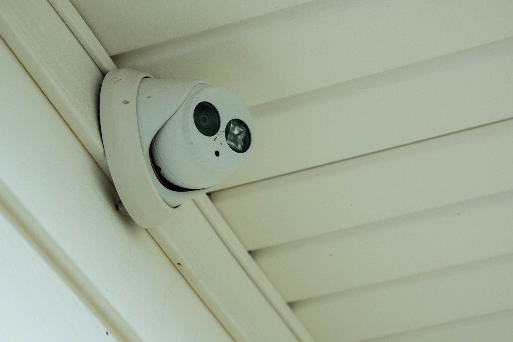 White security camera mounted under an eave, angled downward over a building exterior