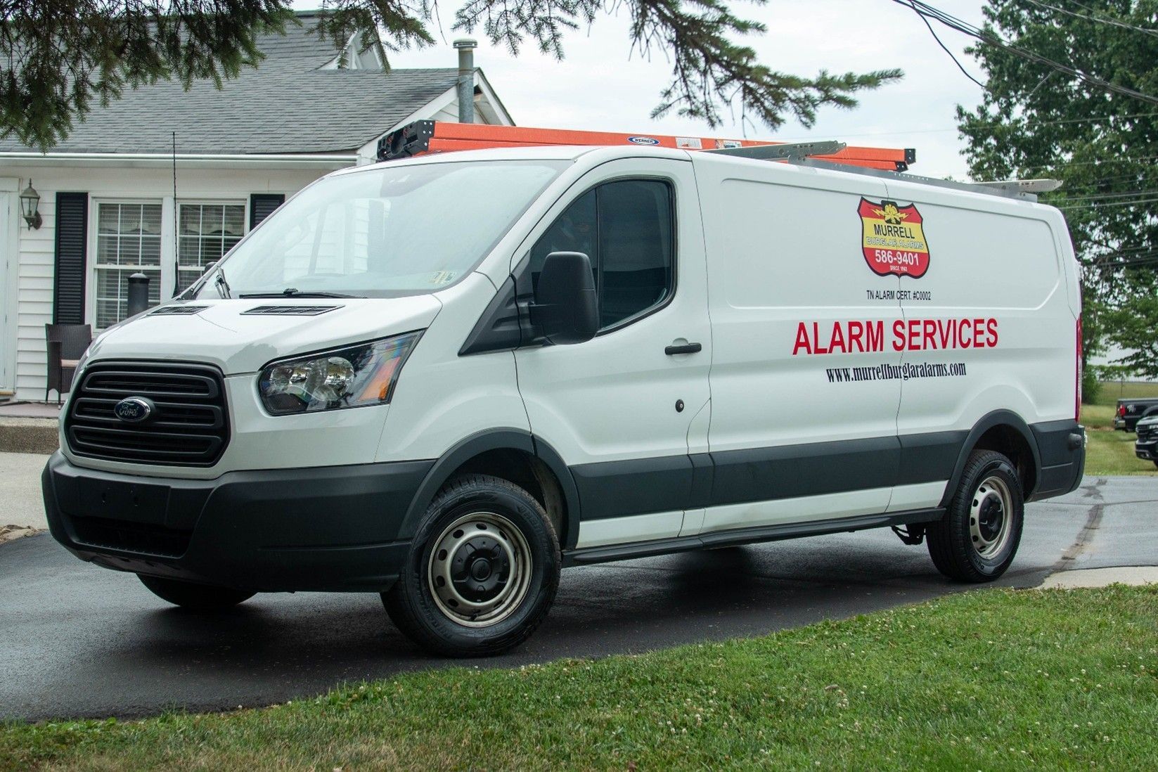White alarm service van parked on a street in front of a house