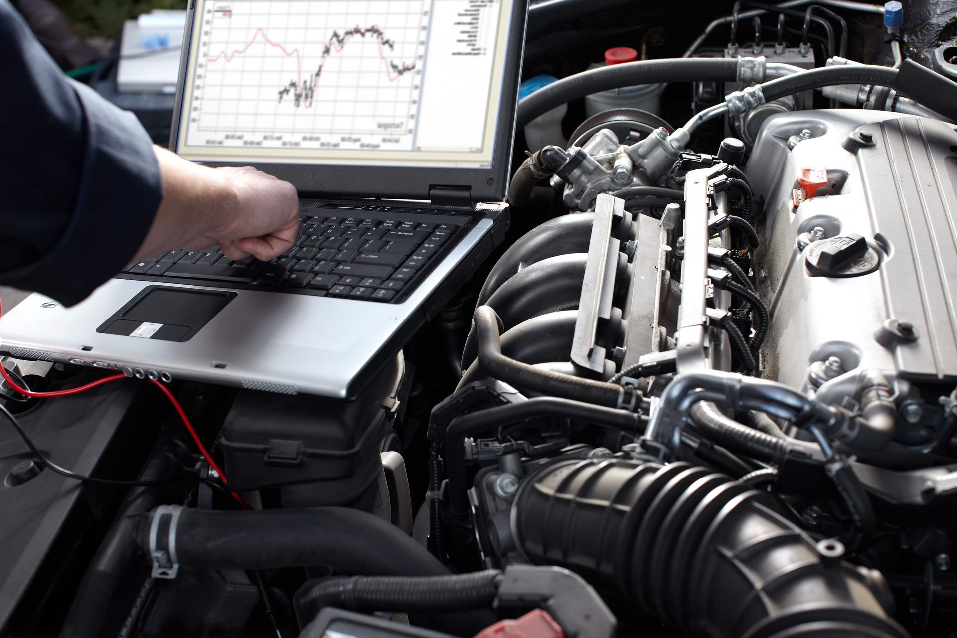 A man is working on a car engine with a laptop.