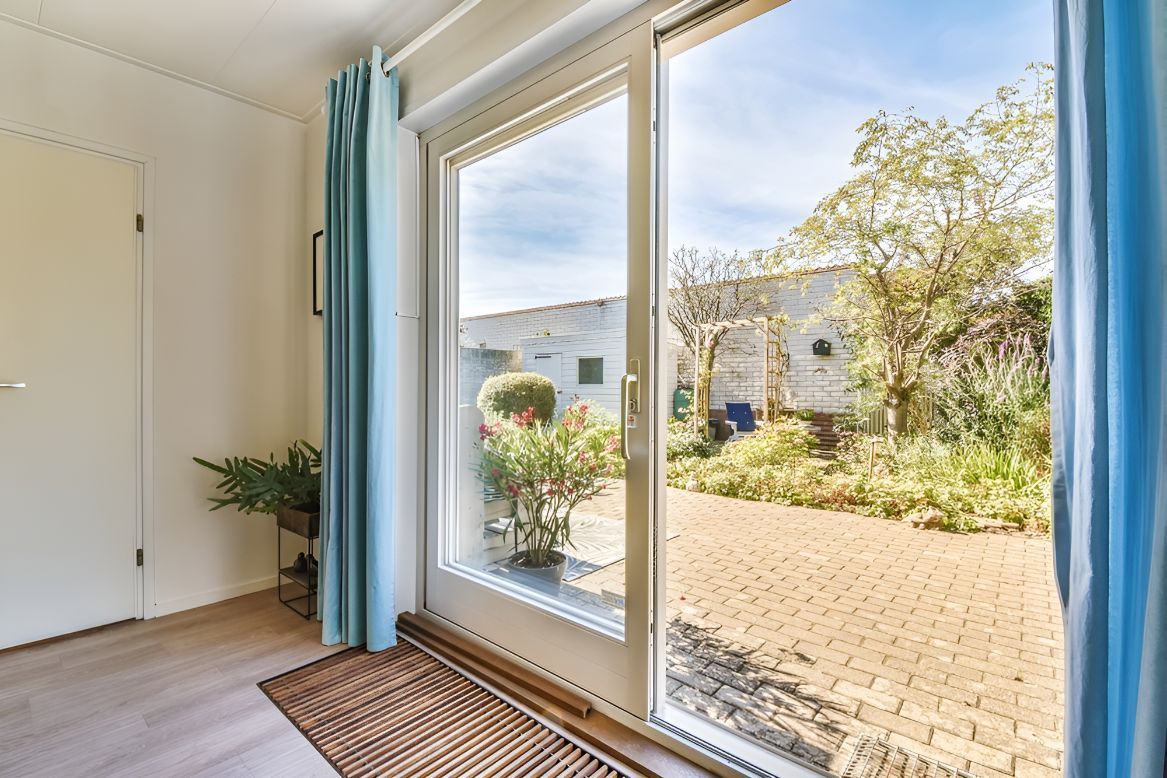 A Large glass window and a white door leading out to a paved patio with trees — Twin Cities Glass In Albury, NSW