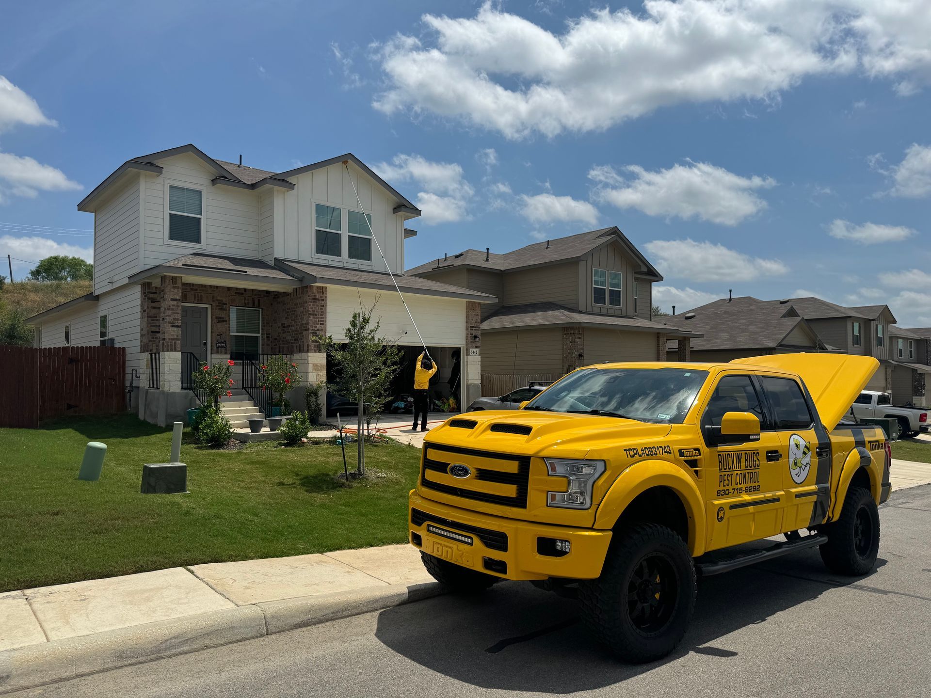 A yellow truck with the hood open is parked in front of a house.
